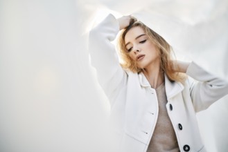 Young attractive woman in white clothes posing on abstract pale background looking at camera