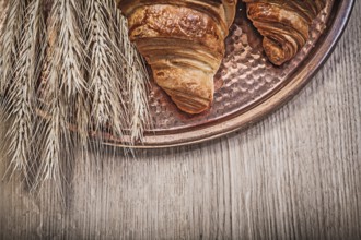 Composition of wheat rye ears freshly baked croissants Copper tray on wooden board