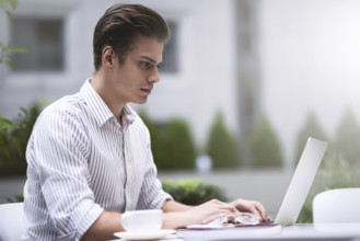 Smart attitude. Positive handsome man using a laptop and sitting in the cafe while surfing the