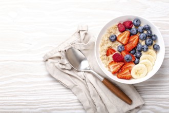 Oatmeal porridge with fruit and berries in bowl with spoon on white wooden background table top