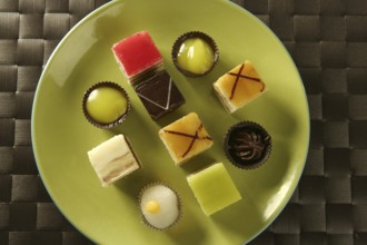 Varied pastries in green dish. Little colorful cakes