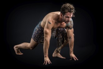 Handsome shirtless muscular man in briefs, covering with long elegant scarf, kneeling, isolated on