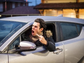Aggressive man driving car and screaming away while showing obscene gesture on street