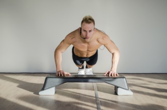 Young aerobics male coach shirtless leaning on step teaching class, looking at camera