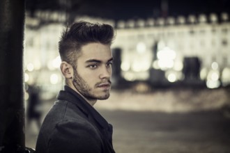 Attractive young man portrait at night with city lights behind him in Turin, Italy, Europe
