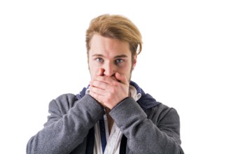 Young blond man covering his mouth while looking at camera against of white background