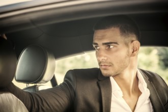 Handsome Young Man Driving a Car, wearing black jacket, hand on wheel