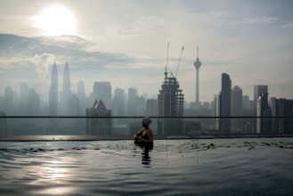 Woman enjoying cityscape of Kuala Lumpur from rooftop swimming pool. Urban scene with skyscrapers,