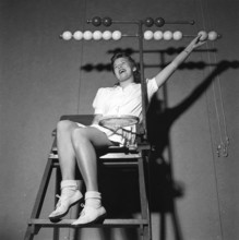 Tennis in the 1940s. A young woman is sitting in the tennis jugdge's chair. The wooden balls in