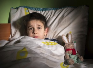 Sick child in bed with teddy bear. Measuring the temperature with a thermometer