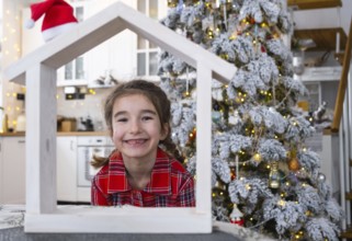 Happy child with tiny house in cozy home with Christmas decor of festive white kitchen. Gift for