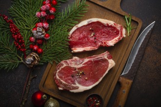 Two raw uncooked meat beef steaks on wooden cutting board with knife and seasonings on dark rustic