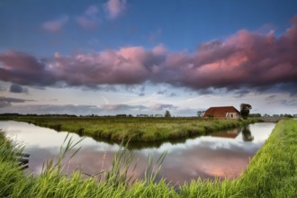Farmhouse and river at dramatic pink sunset, Netherlands