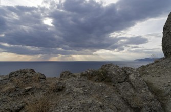 The rays of the sun over the sea make their way through the clouds.Cape Meganom, Crimea,