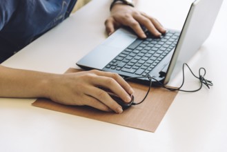 Young man working with laptop, hands on notebook computer and mouse. Blurred background. Student