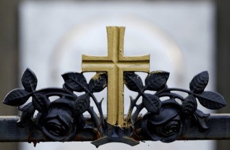 Golden cross on a wrought-iron fence of a grave in a cemetery