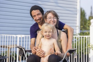 Happy young family pose for group portrait seen from the front. Mother sitting on chair with two