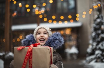 Portrait of joyful girl with a gift box for Christmas on a city street in winter with snow on a