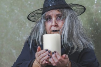 Old white-haired white-haired witch dressed in black with a hat and a large white candle in her