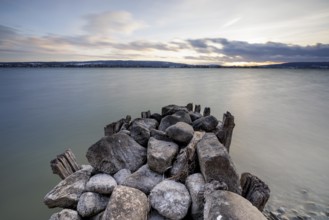 Stone pier jutting into a calm lake, atmospheric clouds in the sky at dusk, calm atmosphere,