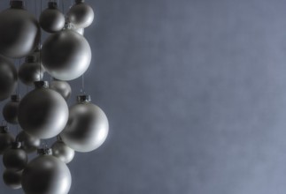 Silver Christmas balls hanged with silver thread, of a matte color, on a gray blurry backdrop,