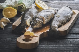 Close-up image with fresh trout displayed on a wooden cutting board, seasoned with garlic and lemon