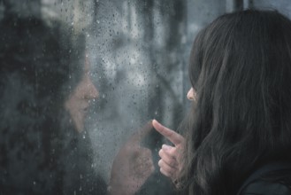 Brunette young woman and her reflection on a window covered with raindrops