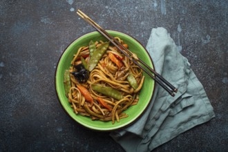 Asian dish stir fry udon noodles with chicken, vegetables and mushrooms in green ceramic bowl with
