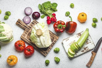 Fresh various vegetables with wooden cutting boards and knife on white kitchen table top view.