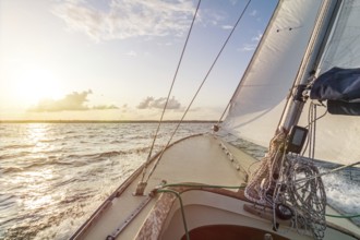 Sailing boat sailing fast into the beautiful sunset during choppy sea
