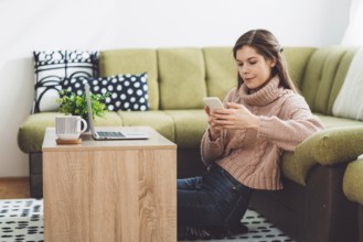 Young caucasian woman with long brown hair in pastel pink sweater and jeans working from home on