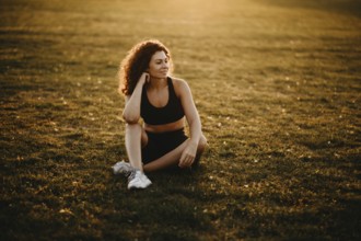 A woman sits on the grass in a field, enjoying a serene sunset