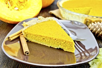 A piece of pumpkin pie in a brown plate with a fork and cinnamon, pumpkin, cones and maple leaf on