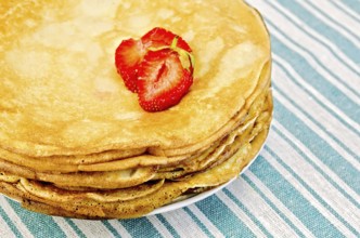 Pancakes stacked on a plate with strawberries on a green striped napkin