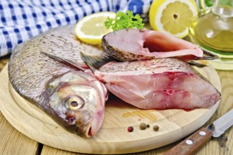 Bream whole peeled and sliced pieces on a round board, parsley, lemon, vegetable oil, napkin, knife