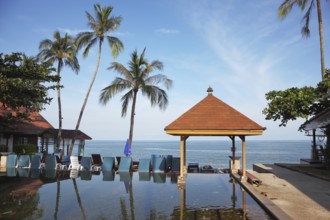 The palm tree and beach armchairs are reflected in a smooth water surface. Pool on a beach of the