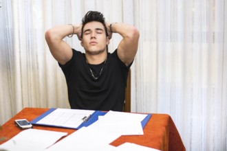 Tired, exhausted or despondent young man sitting at a table with a folder of paperwork leaning
