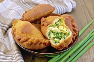 Dish with fried patties with onions and egg, napkin, a bunch of spring onions on a wooden boards