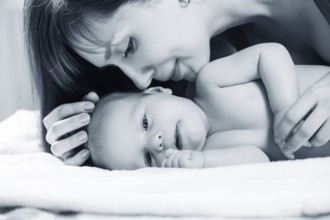 Closeup portrait of cheerful young mother with adorable newborn baby having fun at home, child