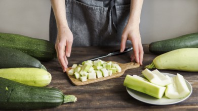 Zucchini harvest. Woman slices zucchini cubes for freezing on wooden table. Farm organic zucchini