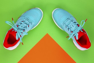Red, cyan, white pair of new tennis shoes in studio shot over green and orange background. Directly