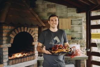 Smiling chef holding big platter with grilled vegetables.