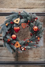 Christmas wreath of fir branches with red Christmas decorations on a stone wall.