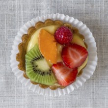 A cake with cream and mixed fruit, resting on linen tablecloth