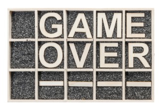 In a collecting box with black decorative sand arranged plywood letters the word GAME OVER stacked