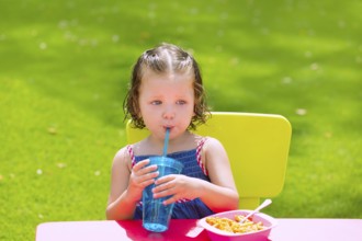 Toddler kid girl drinking eating macaroni pasta in garden turf grass outdoor