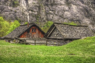 Rustic House with Stone Roof and Green Grass in Front of a Mountain wall in Ticino, Switzerland,