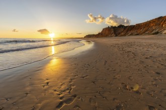 Beautiful sandy beach with red rocks and cliffs. Twilight at sunset with shallow waves on the