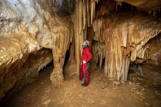 A speleologist with helmet and headlamp exploring a cave with rich stalactite and stalagmite