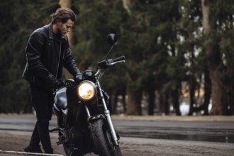 Man in leather jacket with motorcycle on a forest road, evoking a moody, autumn atmosphere